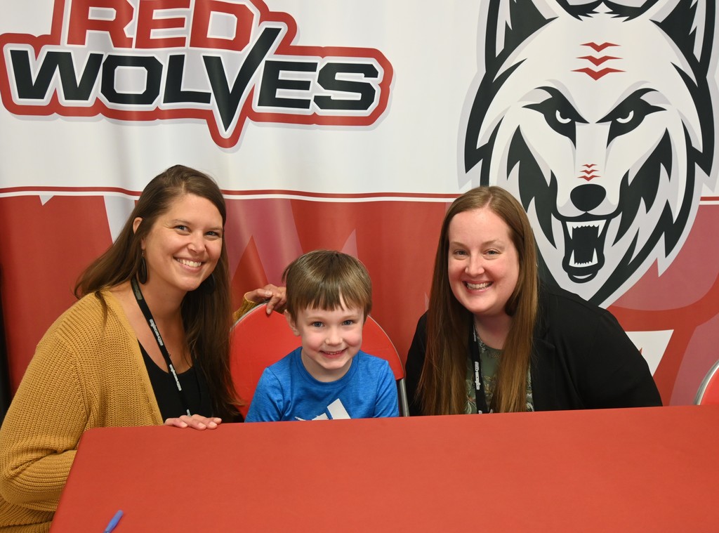 principals with student seated in front of red wolves backdrop
